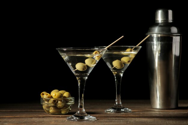 Martini in un bicchiere di vino con olive verdi su uno spiedino su un tavolo di legno marrone. cocktail. sbarra