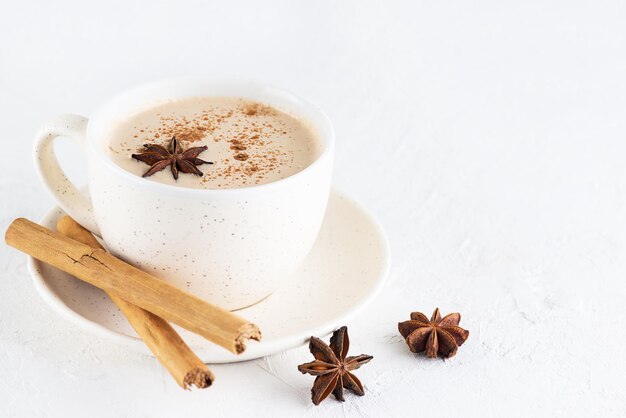 Masala chai con latte di cocco e spezie in una tazza su un tavolo bianco. Messa a fuoco selettiva.