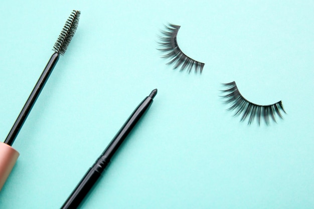 Mascara black eyeliner and false eyelashes on color background