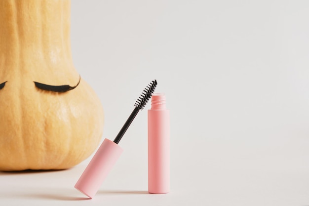 Mascara in mock up confezione rosa vuota e zucca con ciglia finte su sfondo grigio spazio copia autunno, stagione autunnale make up concept