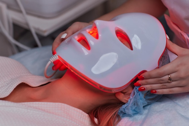 Maschera antietà a luce LED per la cura della pelle del viso in una spa al rallentatore Una donna sdraiata su un divano in una maschera speciale Moderne tecnologie di bellezza e salute