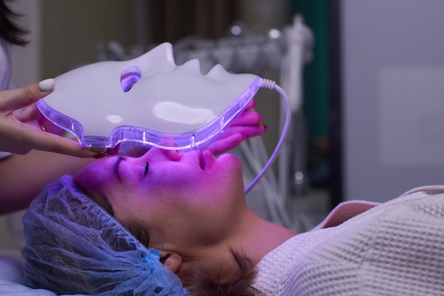 Maschera antietà a luce LED per la cura della pelle del viso in una spa al rallentatore Una donna sdraiata su un divano in una maschera speciale Moderne tecnologie di bellezza e salute