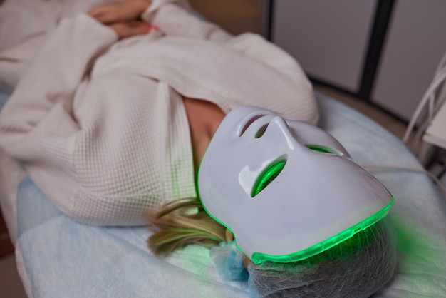 Maschera antietà a luce led per la cura della pelle del viso in una spa al rallentatore una donna si trova su un divano in una specifica