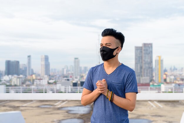 Maschera d'uso del giovane multi etnico con le mani giunte contro contro la vista della città