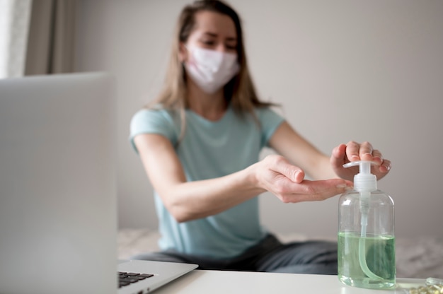 Maschera d'uso della donna dentro e usando disinfettante per le mani