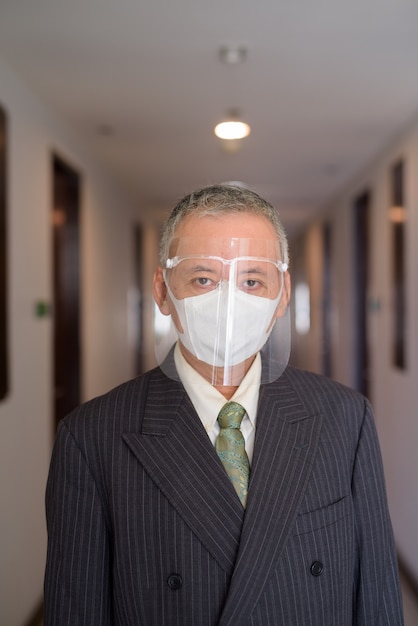 Maschera d'uso e maschera facciale dell'uomo d'affari giapponese maturo nel corridoio