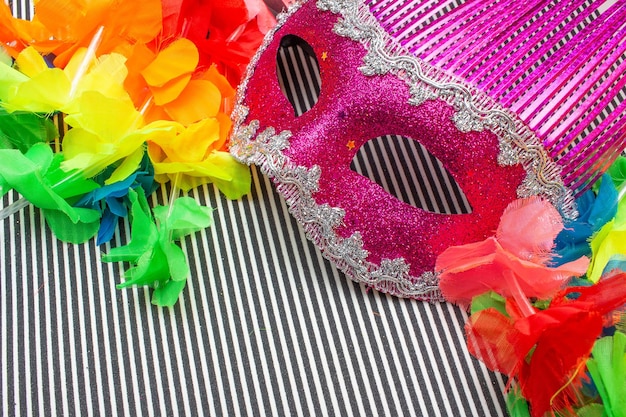 Maschera di carnevale rosa su sfondo a strisce bianche e nere e fiori colorati