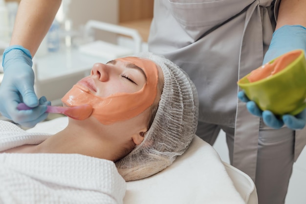 Maschera di gelatina cosmetica cosmetologo per la cura della pelle del viso applica maschera di alginato con spatola sul viso