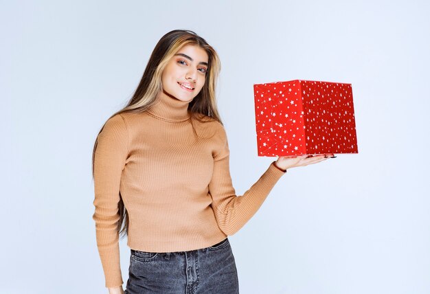 Maschera di un modello attraente della donna che tiene un presente rosso.