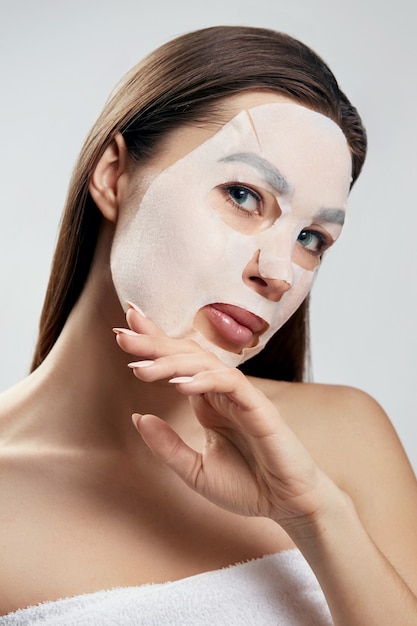 Maschera facciale di bellezza. Donna con una maschera idratante in panno sul viso. Cura della pelle. Maschera termale cosmetica. Trattamento facciale