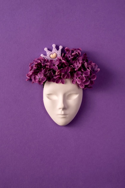 Maschera facciale in plastica decorata con fiori lilla e corona in miniatura su sfondo viola