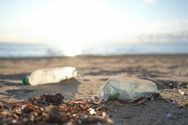 Maschera facciale medica e bottiglia di plastica gettate sulla costa sporca per l'inquinamento causato dalla pandemia di COVID-19