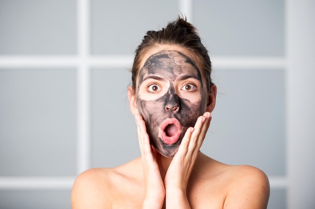 Maschera facciale per la cura della pelle donna che applica maschera di argilla nera isolata a casa il giovane modello spa utilizza la cura del viso