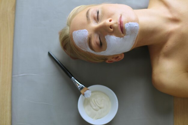 Maschera faccialebella ragazza alla spa estetista donna che applica maschera facciale