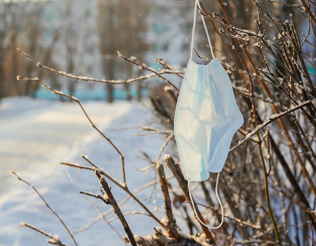 Maschera medica in inverno su un ramo di un albero, vicino alla strada