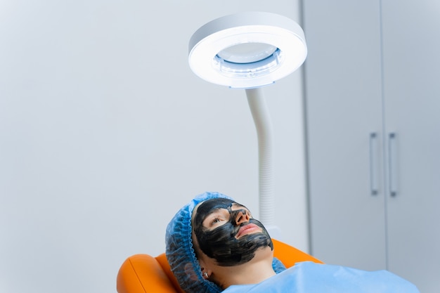 Maschera nera sul viso della ragazza per il peeling al carbonio. Dermatologia e cosmetologia. Usando il laser chirurgico.