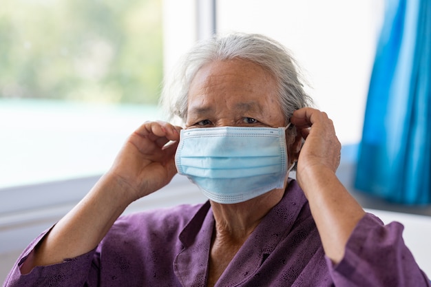 Maschera per il viso d'uso della donna asiatica senior durante il virus della corona e l'epidemia di influenza. Protezione da malattie e malattie. la paziente anziana che è a rischio di infezione da virus corona [covid-19].