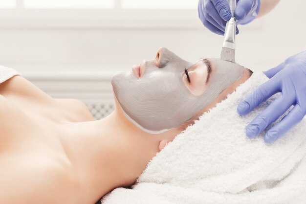 Maschera per il viso, trattamento di bellezza spa, cura della pelle. Donna che ottiene maschera nutriente facciale dall'estetista al salone della stazione termale, vista laterale, primo piano