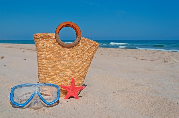 Maschera subacquea con borsa di paglia e stelle marine sulla spiaggia