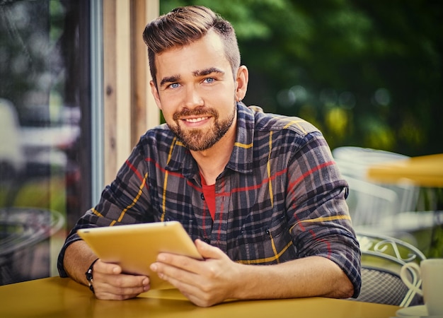 Maschio barbuto bello dei pantaloni a vita bassa che utilizza il computer portatile in un caffè.