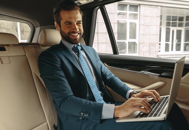 Maschio caucasico barbuto bello che ride del computer portatile in auto