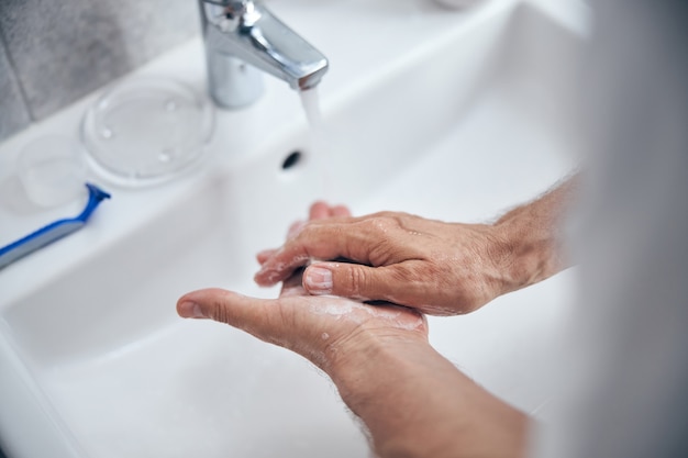 maschio che si sfrega i palmi delle mani con il sapone su un lavandino in ceramica