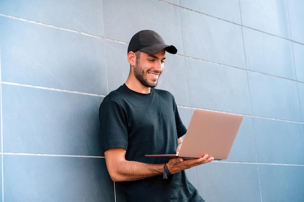 Maschio felice che utilizza laptop vicino al muro