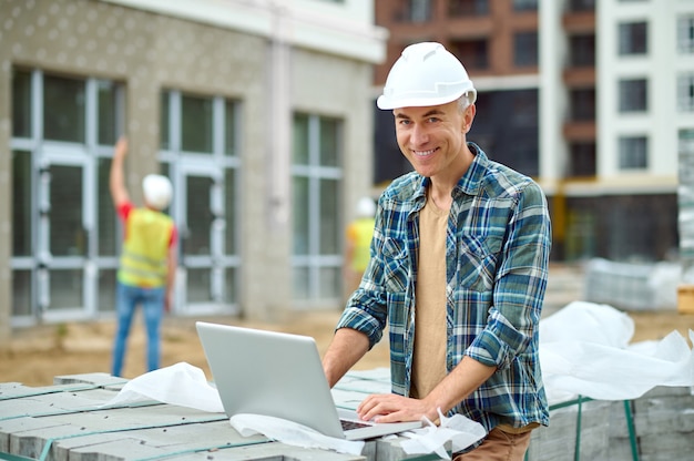 Maschio gioioso che lavora al suo laptop in cantiere