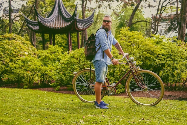 Maschio hipster barbuto rosso su una bicicletta retrò in un parco estivo.