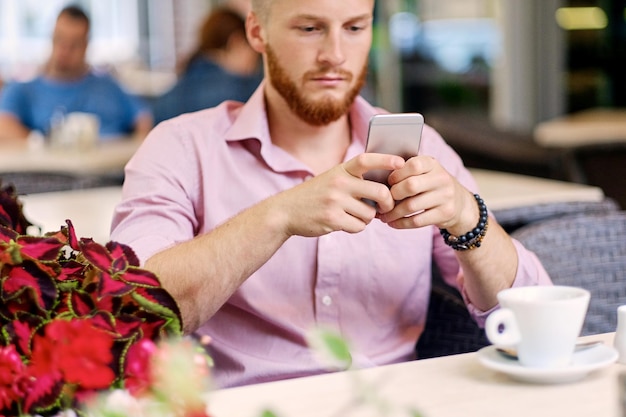 Maschio rosso casual che utilizza uno smartphone in un caffè in una strada.