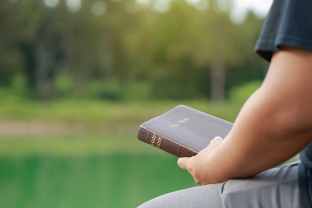 Maschio seduto e tenendo la Bibbia in mano con lo sfondo della natura. Letture domenicali, Bibbia