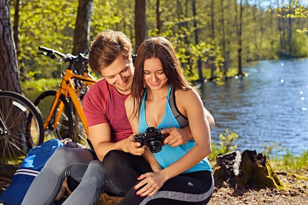 Maschio sorridente che mostra le immagini dei giri in bicicletta alla sua ragazza sulla costa selvaggia del fiume.