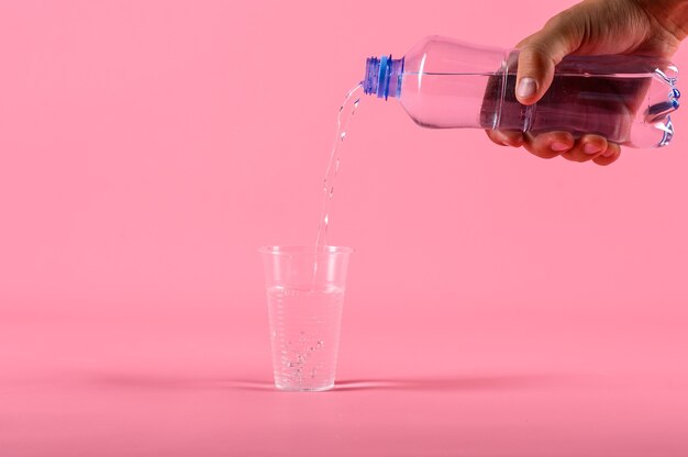 Maschio versando acqua dalla bottiglia in un bicchiere di plastica su sfondo rosa