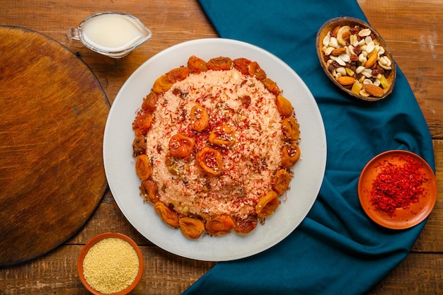 Masfouf di cous cous con frutta secca e noci su un tavolo di legno accanto a zafferano e granella di cous cous