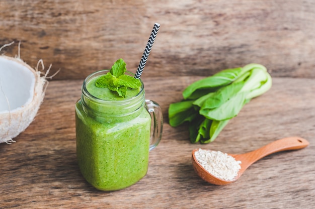 Mason jar tazze riempite con spinaci verdi, banana e frullato di latte di cocco con un cucchiaio di farina d'avena sul tavolo