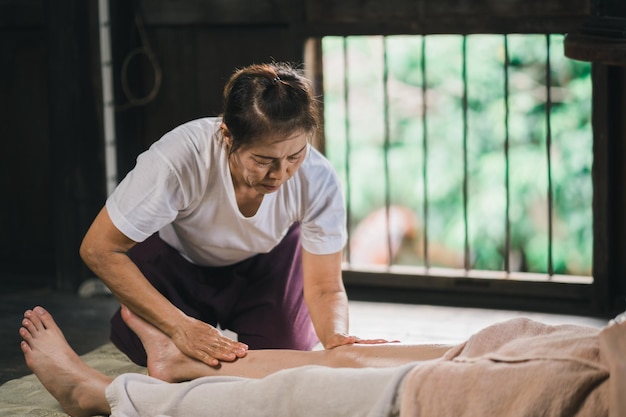 Massaggi e spa trattamento rilassante della sindrome dell'ufficio con pietre calde tradizionali massaggio tailandese stile Asain massaggiatrice femminile che fa massaggio ai piedi cura lo stress per la donna