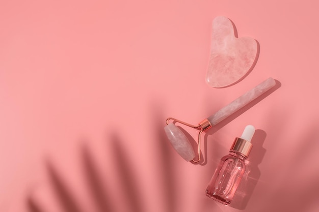 Massaggiare il rullo di quarzo e la bottiglia di vetro rosa di gel trasparente liquido cosmetico su sfondo rosa