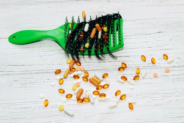 Massaggiare la spazzola verde chiaro con i capelli caduti con vitamine su uno sfondo di legno