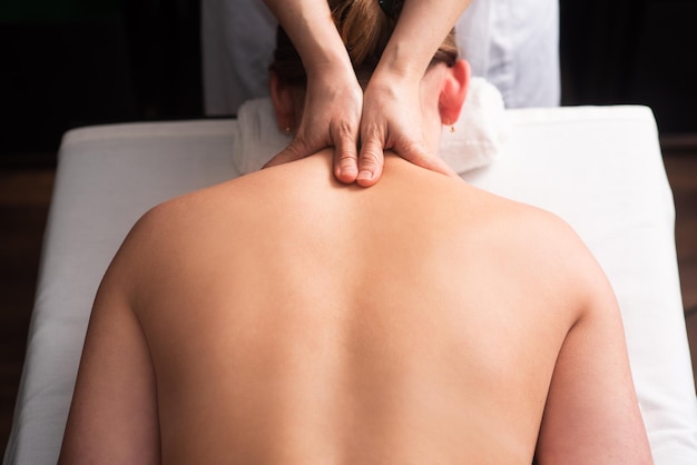 Massaggiatore che massaggia la schiena e le scapole della giovane donna sul lettino da massaggio Concetto di massaggi trattamenti termali Primo piano