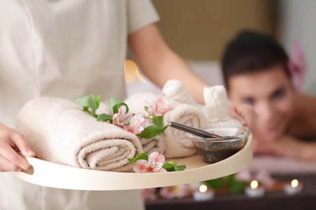 Massaggiatore femminile che tiene vassoio con prodotti di terapia termale nel centro benessere