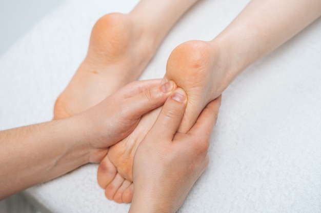 Massaggiatore maschio che massaggia i piedi alla giovane donna rilassante sdraiata sul lettino da massaggio closeup