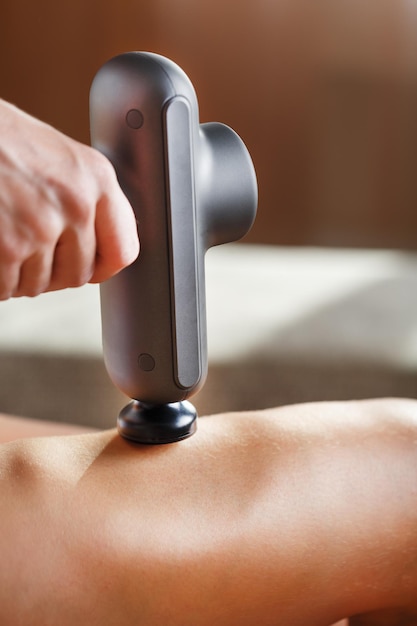 Massaggio delle gambe delle donne con un dispositivo di massaggio d'urto. Automassaggio d'urto per ripristinare i muscoli della fascia e i punti trigger