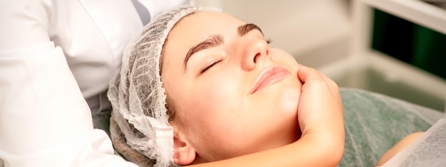 Massaggio facciale Mani di un massaggiatore che massaggia il collo di una giovane donna caucasica in un salone termale il concetto di massaggio salutare