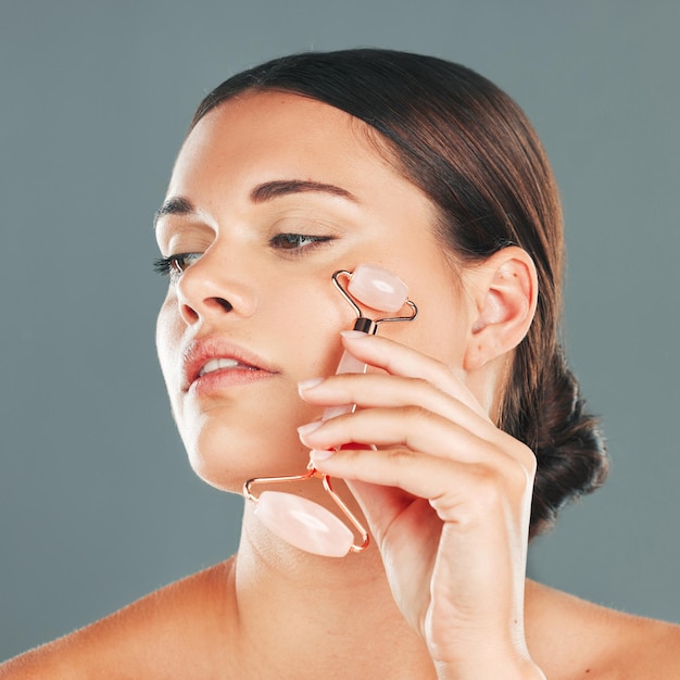 Massaggio viso primo piano con rullo donna e cura della pelle bellezza e pelle sana isolata su sfondo studio Cosmetici naturali bagliore e strumenti per il trucco al quarzo rosa in mano manicure e cura cosmetica