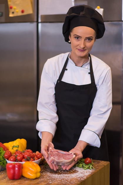 Master Chef che tiene una succosa fetta di bistecca cruda con verdure intorno su un tavolo di legno