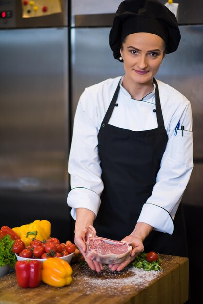 Master Chef che tiene una succosa fetta di bistecca cruda con verdure intorno su un tavolo di legno