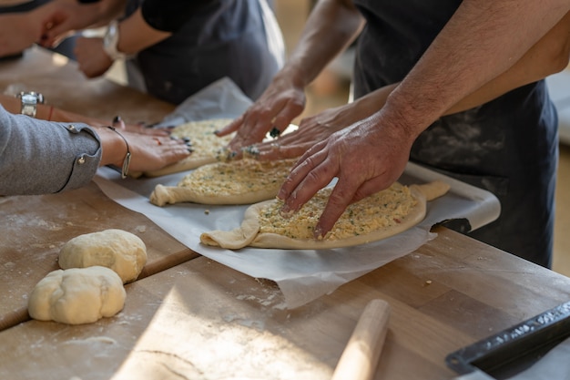 Master class culinaria. Primo piano delle mani della gente che preparano khachapuri. Pane tradizionale georgiano al formaggio. Cibo georgiano