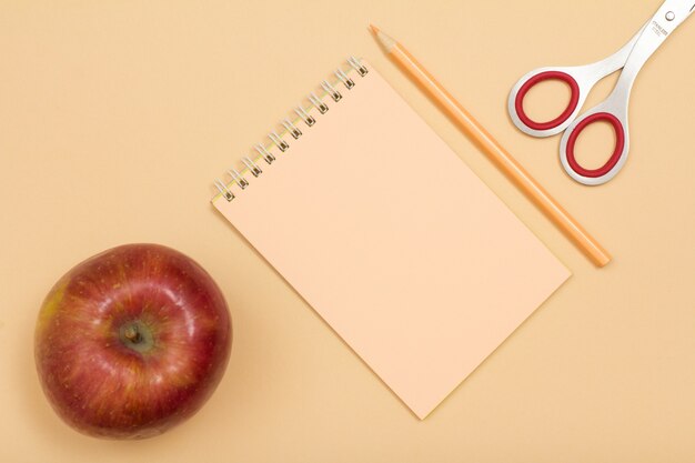 Materiale scolastico. Apple, taccuino, matita colorata e forbici su fondo beige. Vista dall'alto con copia spazio. Torna al concetto di scuola. Colori pastello