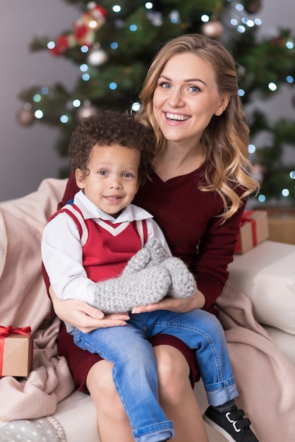 Maternità felice. Bella affascinante donna bionda seduta sul divano e avere suo figlio in grembo mentre celebrava il Natale