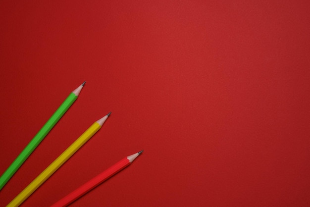 Matite di legno colorate sparse sul concetto di educazione sfondo rosso